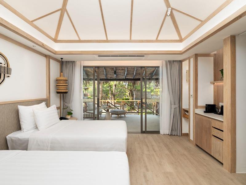 Modern hotel room with two beds, wooden floor, and view of a terrace with garden.