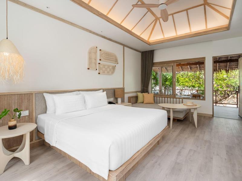 Bright hotel room with double bed, modern furniture, and access to a garden area.