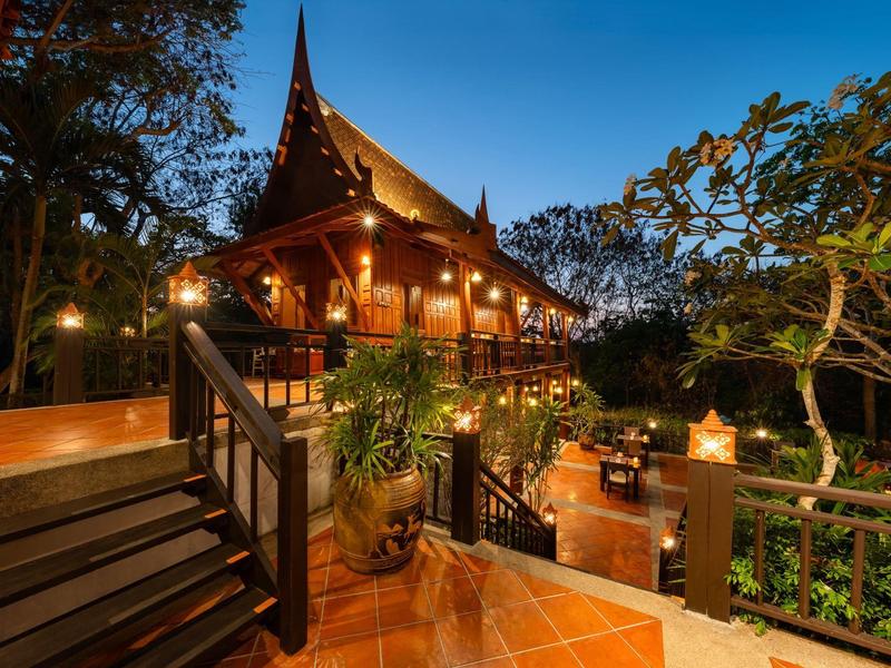 Traditional wooden house with warm lights surrounded by lush vegetation at dusk.