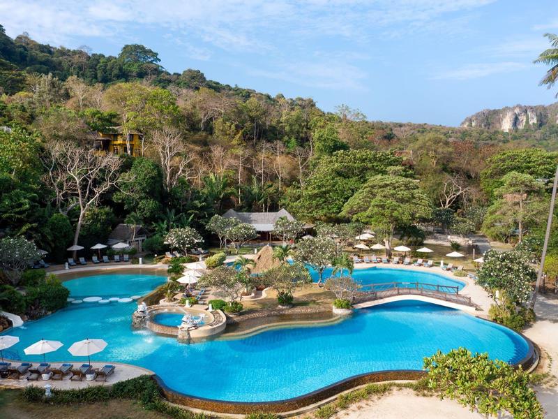 Large resort pool with an island in the center, surrounded by lounge chairs and green hills.