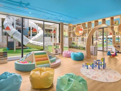 Sala giochi per bambini colorata con scivolo, pouf e diverse aree gioco.