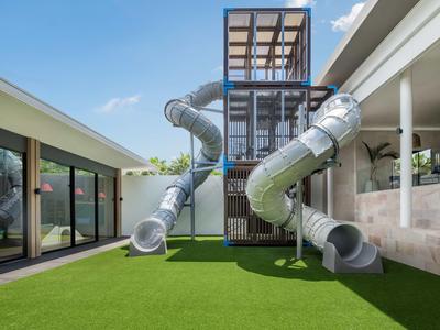 Parco giochi moderno con grandi scivoli a tubo su prato artificiale verde tra edifici.