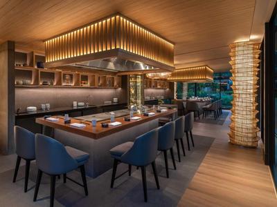 Area ristorante moderna con elementi in legno, eleganti sedie blu e illuminazione indiretta.