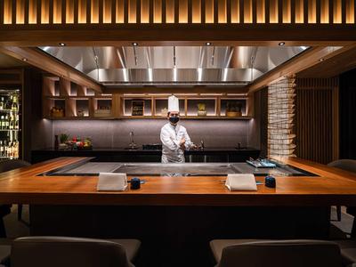 Chef giapponese moderno in esclusivo ristorante teppanyaki con bancone in legno.