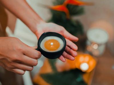 Mani che tengono una piccola candela accesa in un porta candele nero con sfondo sfocato.