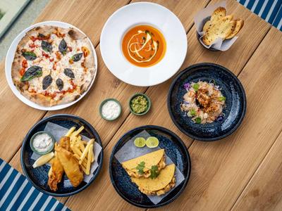 Varie pietanze tra cui pizza, zuppa e pesce con contorni disposte su un tavolo di legno.