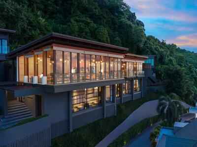 Hotel moderno con grandi finestre di vetro immerso in un paesaggio verde al tramonto.