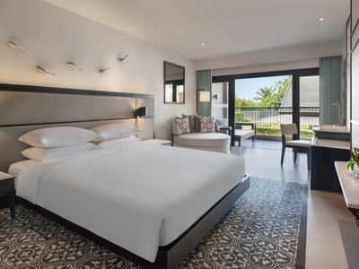 Camera d'hotel moderna con letto grande, zona salotto e vista sulla terrazza e il giardino.