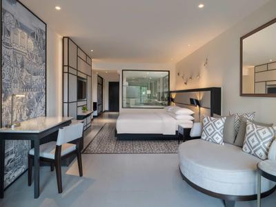 Camera d'hotel moderna con letto matrimoniale, zona salotto e grande specchio a parete.