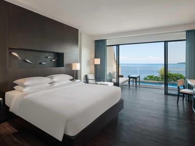 Camera d'hotel moderna con letto grande e vista sul mare tramite una grande parete finestrata.