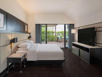 Camera d'hotel moderna con letto matrimoniale, TV e accesso al balcone con vista sul verde.