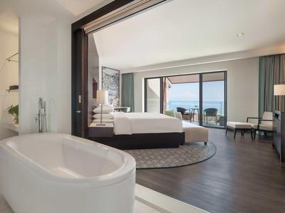 Camera d'hotel moderna con vasca da bagno autonoma, letto matrimoniale e vista mare su pavimento in legno.