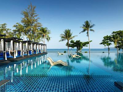 Piscina a sfioro con lettini e palme contro il cielo blu e il mare