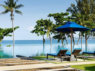 Piscina a sfioro con lettini e ombrellone su spiaggia tropicale con palme.