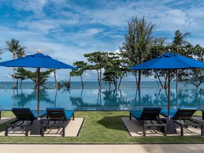 Piscina a sfioro con lettini e ombrelloni blu davanti a un paesaggio tropicale