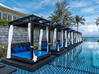 Lussuosi lettini blu accanto a una piscina con vista sul mare e palme.