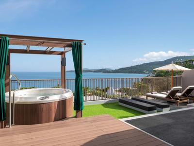 Vasca idromassaggio sulla terrazza con vista sul mare e lettini sotto cielo limpido.