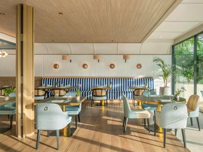 Ristorante luminoso con pavimento in legno, sedie moderne e grandi finestre con vista sul verde.