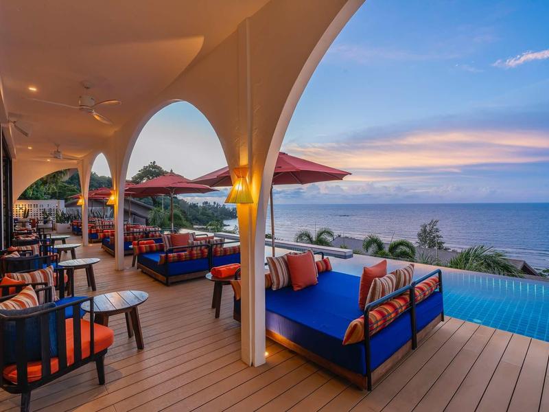 Terrassenbereich mit Sofas und Stühlen, Holzfußboden, Blick auf Pool und Meer bei Sonnenuntergang.