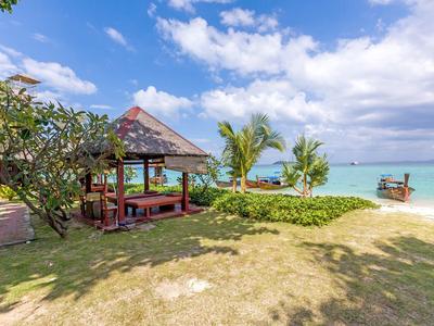 Pavilion with seating and view of tropical beach with clear sky and boat.