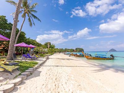 Weißer Sandstrand mit Palmen, bunten Sonnenschirmen und klarem türkisfarbenem Wasser unter blauem Himmel.