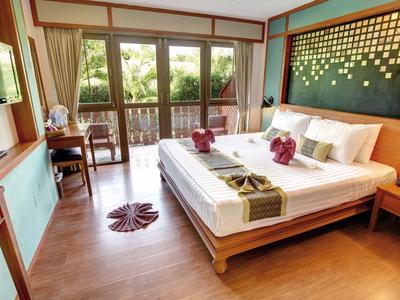 Helles Hotelzimmer mit großem Bett, Holzmöbeln und Balkon mit Blick ins Grüne.