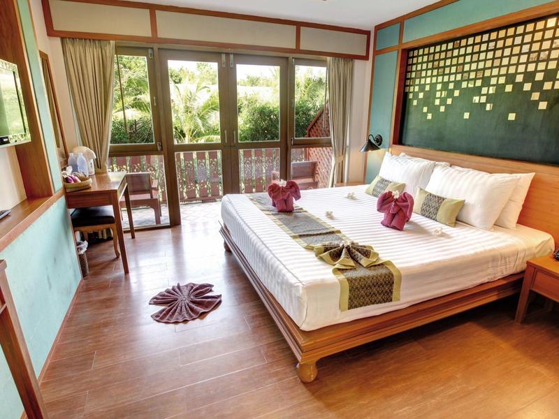 Bright hotel room with double bed, TV, balcony, and greenery view.