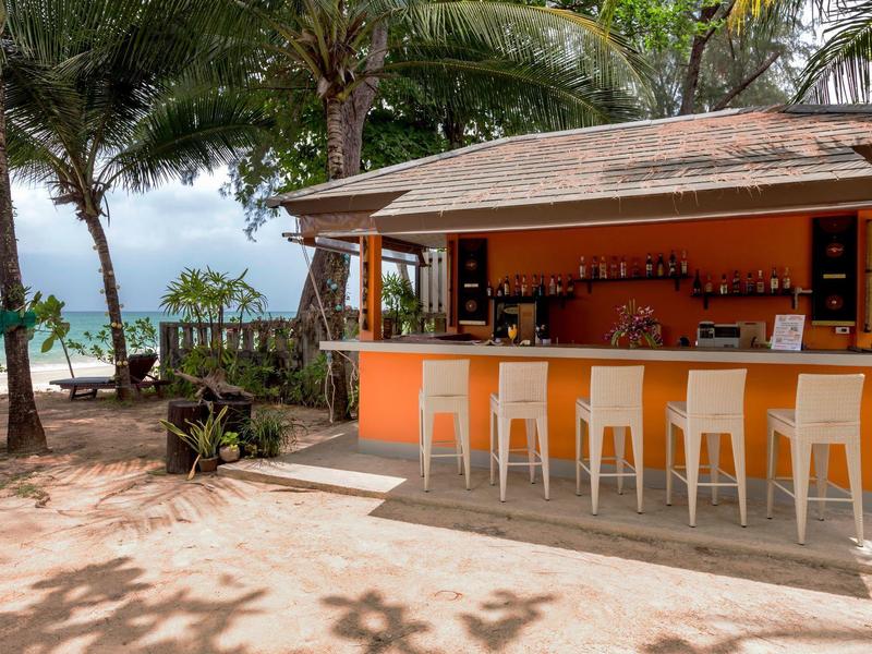 Open beach bar with white bar stools and palm trees on the sandy shore by the sea.
