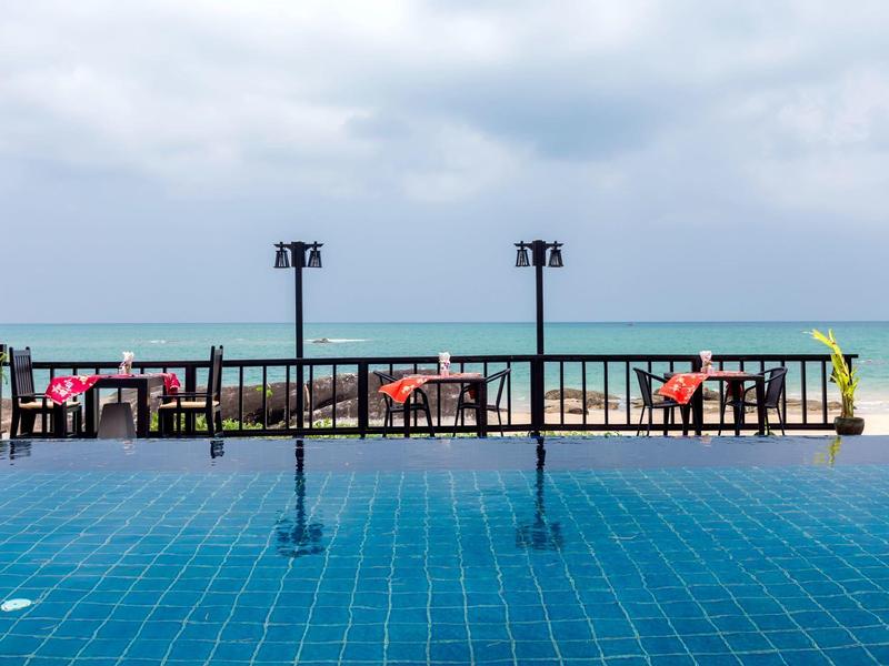 Pool with blue tiled floor, restaurant area with red chairs, and sea view in the background.