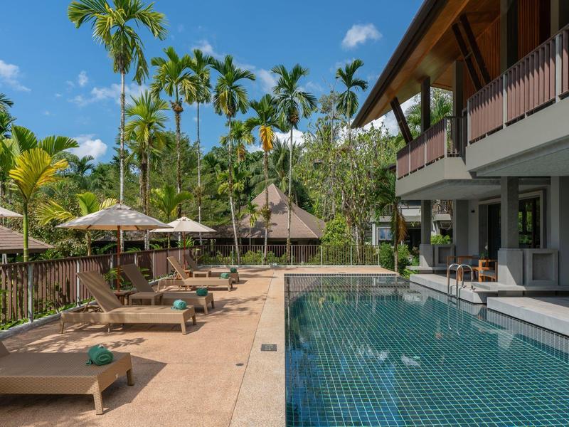 Modern pool with lounge chairs and umbrellas next to a hotel and palm trees.
