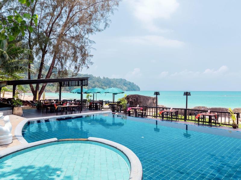 Pool with sea view at a tropical hotel with palm trees and seating areas.
