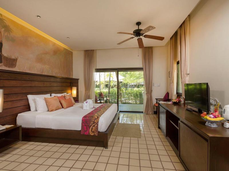 Modern hotel room with large bed, ceiling fan, and view of garden and pool.