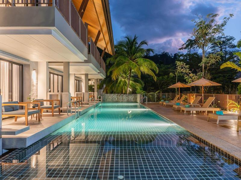 Evening view of a modern hotel with an illuminated pool and outdoor area with palm trees.