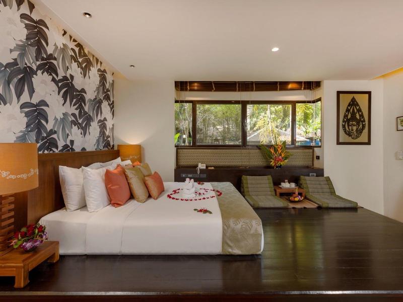 Bright hotel room with large bed, artistic wall design, and seating area with sofas.