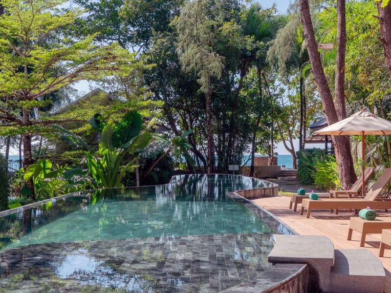 Pool area with lounge chairs, umbrellas, and trees at a tropical hotel.