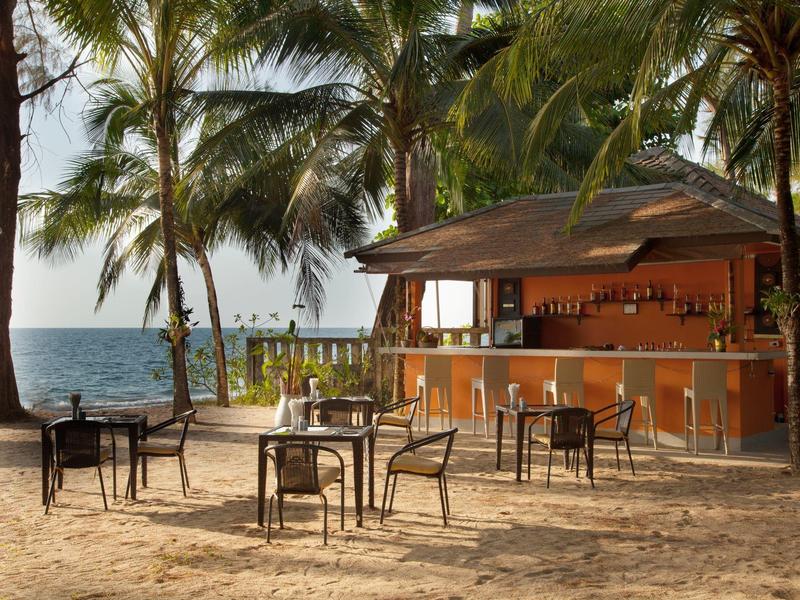 Beach bar with wooden counter and seating areas under palm trees by the sea