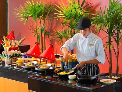 Koch bereitet Essen an Buffet mit vielfältigen Speisen und bunten Töpfen vor.