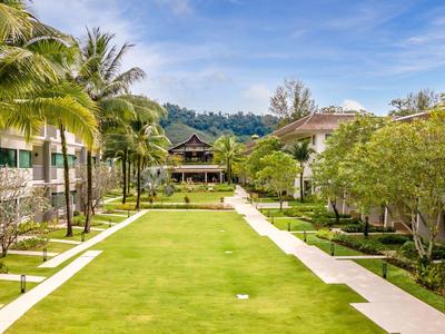 Ein gepflegter Garten mit palmengesäumtem Weg zwischen Hotelgebäuden unter blauem Himmel.