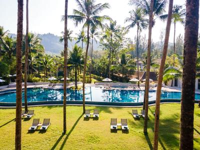 Velký bazén obklopený palmami s lehátky na zelené trávě a horami v pozadí.