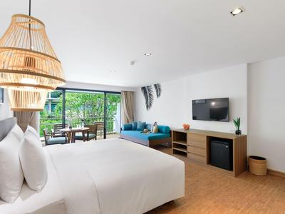 Helles Hotelzimmer mit großem Bett, Rattanlampe, Sofa und Balkon mit Blick ins Grüne.