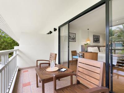 Balkon mit Holztisch und Stühlen neben einem Wohnzimmer mit offenem Schiebetürfenster in einem Hotel