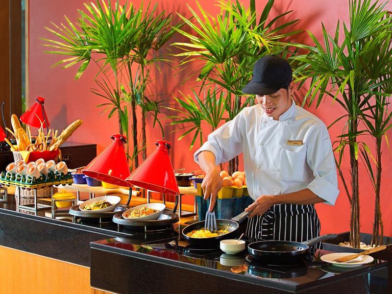 Koch bereitet Essen an Buffet mit vielfältigen Speisen und bunten Töpfen vor.