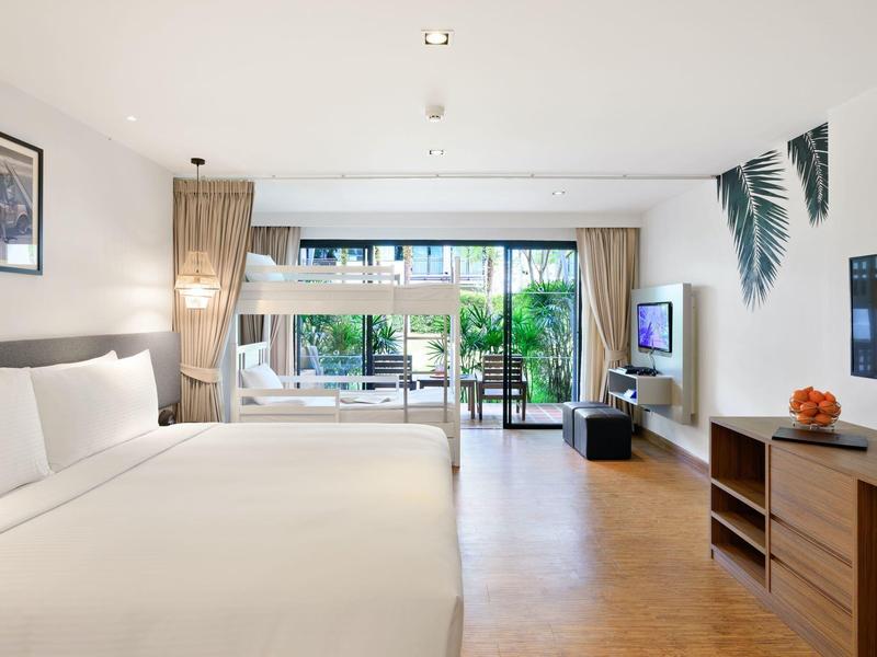 Helles Hotelzimmer mit großem Bett, Sofabett, Holzfußboden und Gartenausblick.