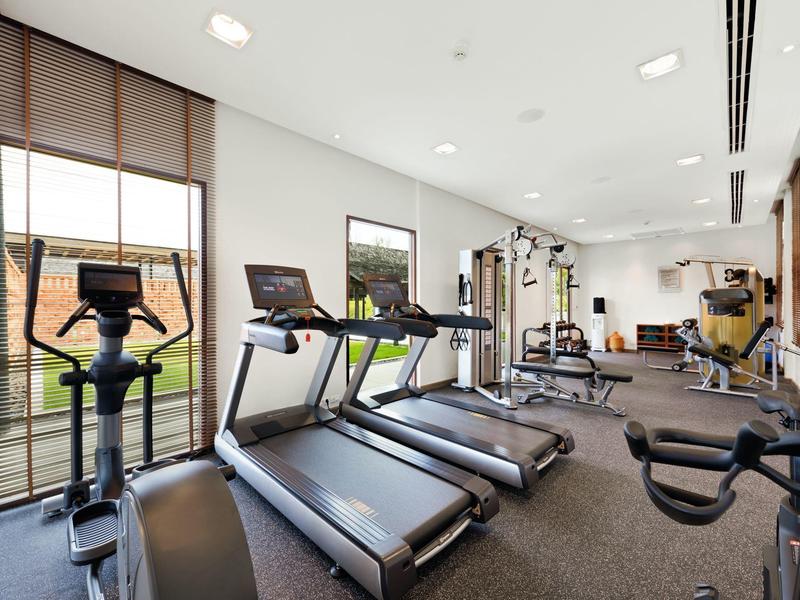 Helle Hotel-Fitnessraum mit Laufbändern und Fitnessgeräten vor großen Fenstern