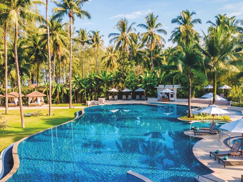Großer Pool in tropischer Hotelanlage mit Sonnenschirmen und Palmen im Hintergrund.