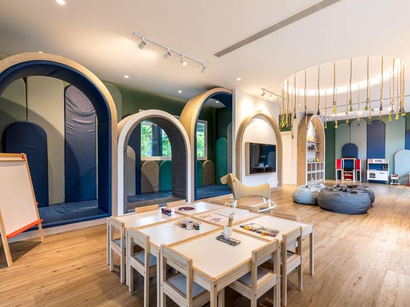 Moderner Kinderspielraum mit Holztischen, Stühlen und bunten Podesten unter großen Rundbögen.