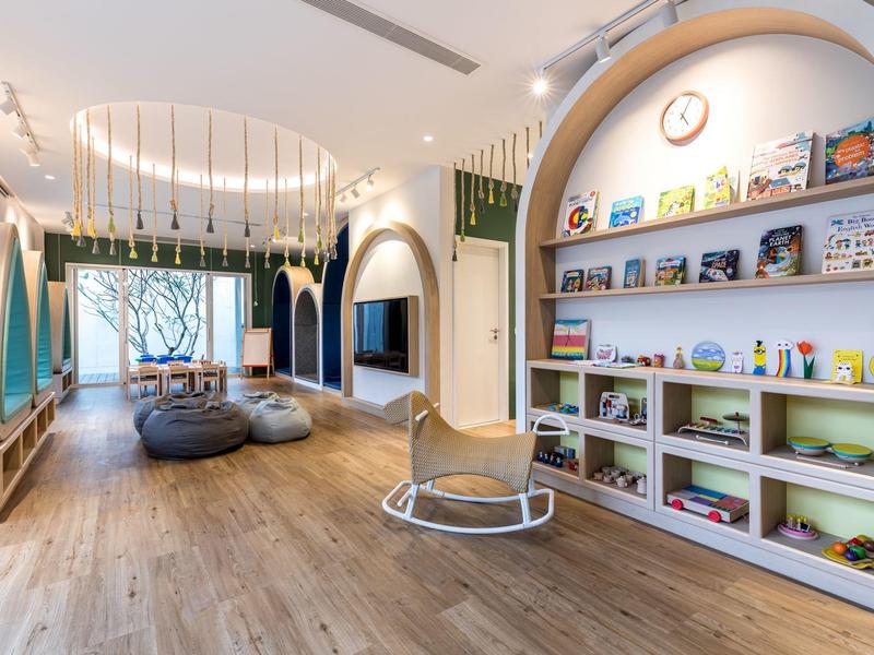 Heller und moderner Kinderspielraum mit Holzfußboden, Bücherregalen und Sitzkissen.