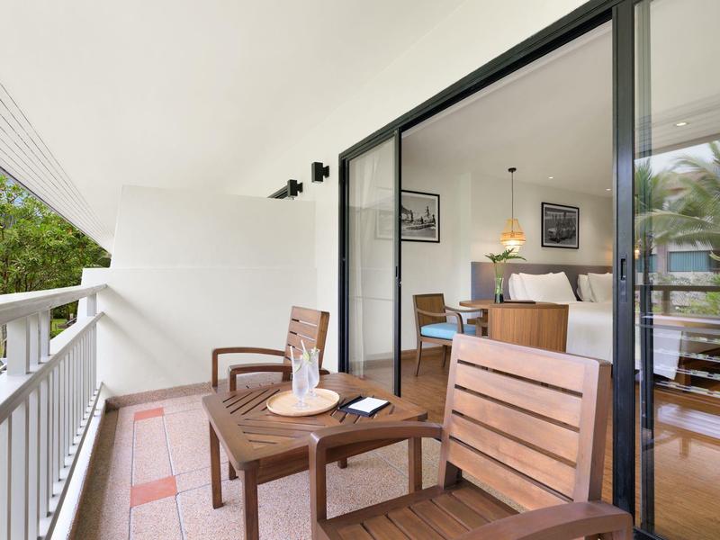 Balkon mit Holztisch und Stühlen neben einem Wohnzimmer mit offenem Schiebetürfenster in einem Hotel