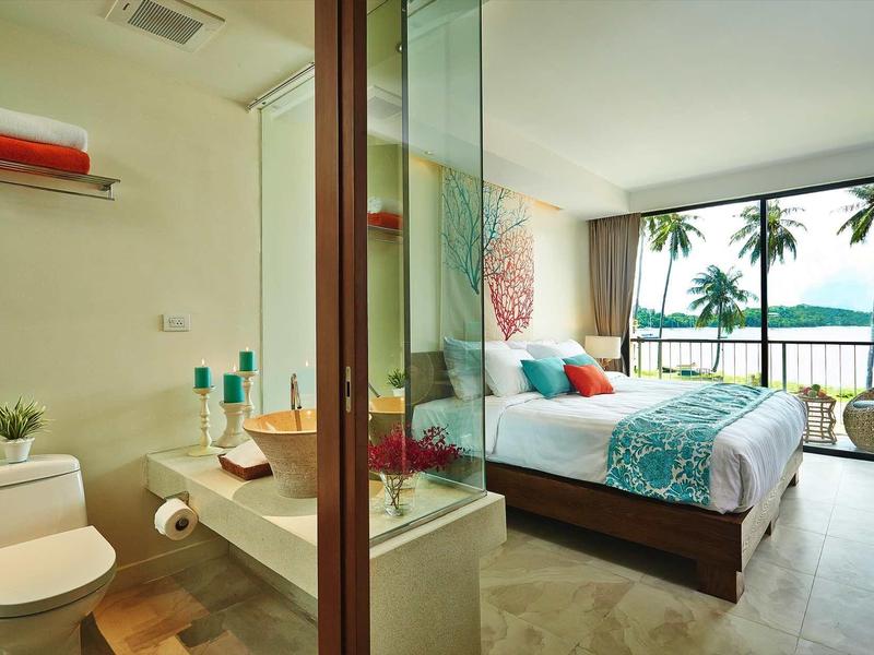 Helles, modernes Schlafzimmer mit Meerblick, Doppelbett und angrenzendem Bad mit Glaswand.