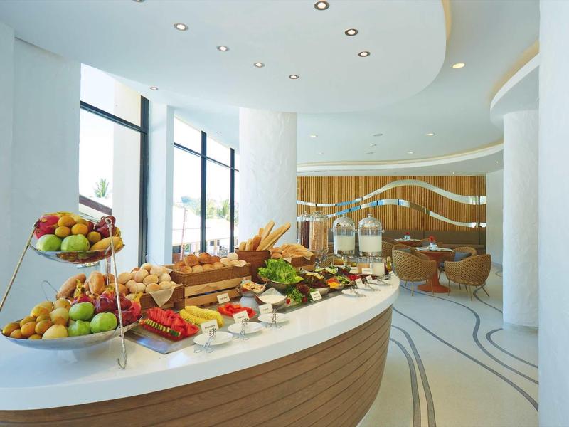 Moderner Buffetbereich mit Obst, Brot und Aufschnitt auf weißer Theke vor großen Fenstern.